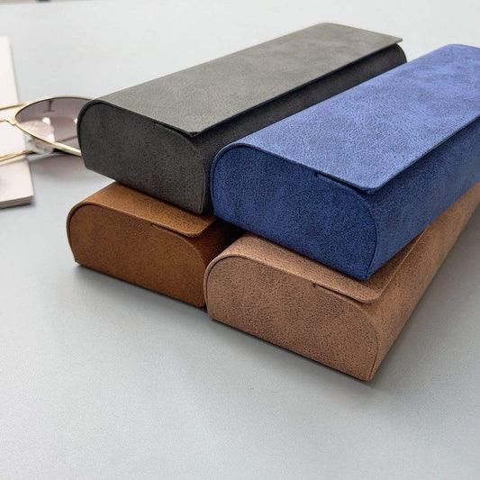 Three rectangular fabric-covered glasses cases in gray, blue, and brown on a light gray surface.