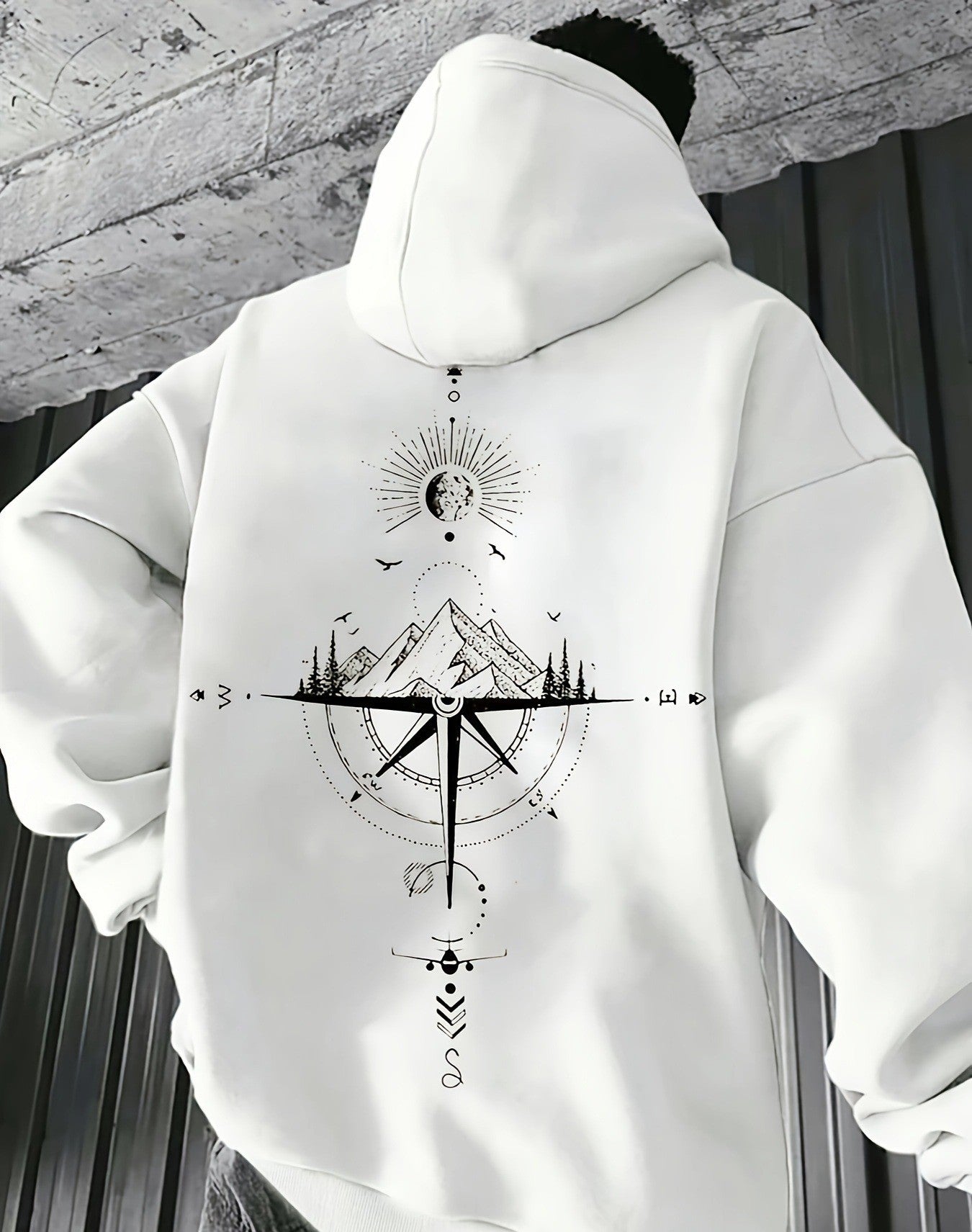 White hoodie with black geometric design worn by a person against a gray concrete wall.