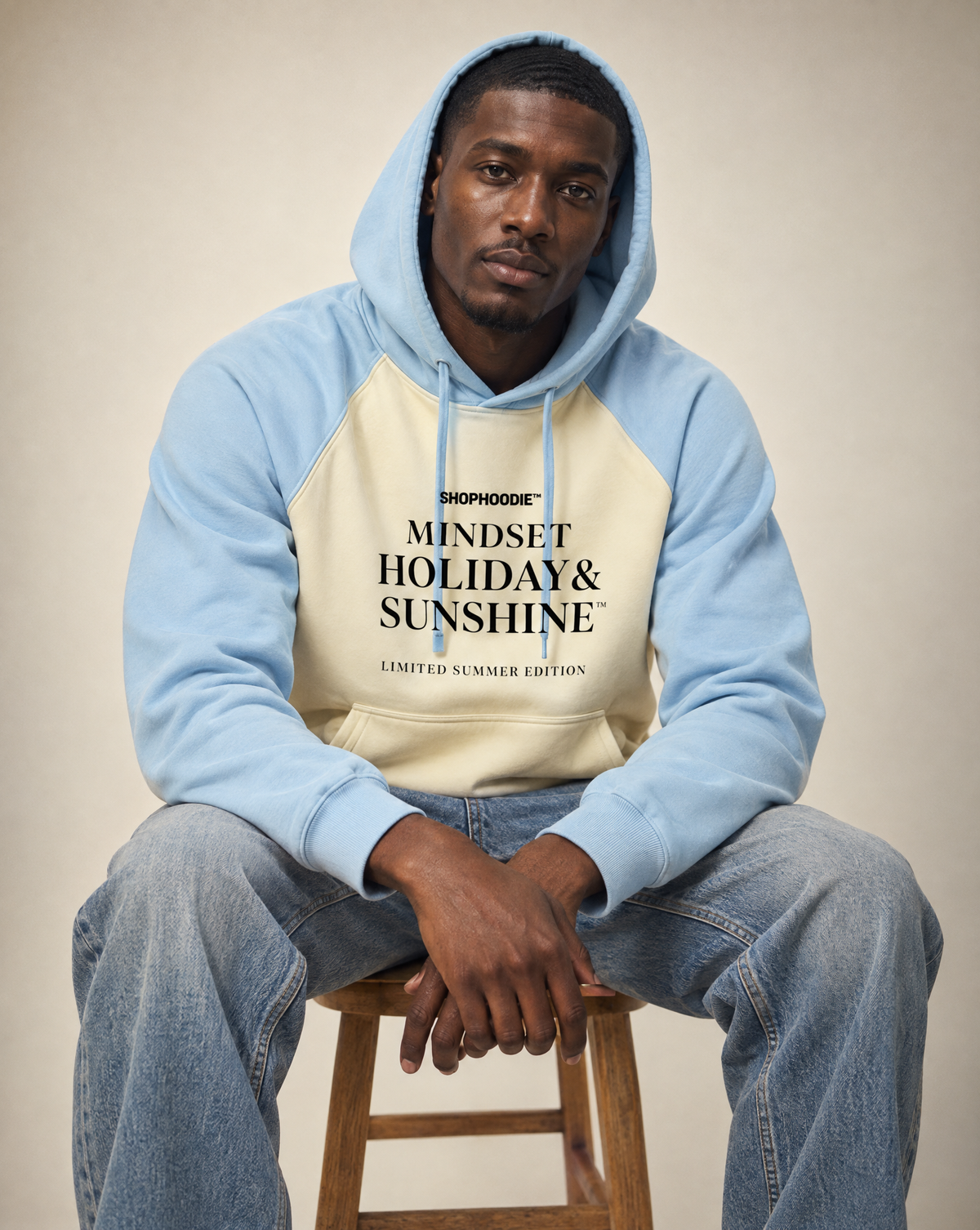 Male model seated wearing the SHOPHOODIE® Mindset Holiday & Sunshine Raglan Hoodie in Mild Apricot with Sky Blue, hood up