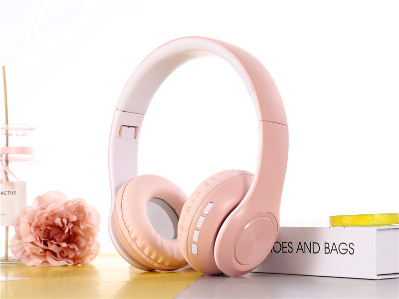 Pink headphones on a white surface with a flower and box in the background