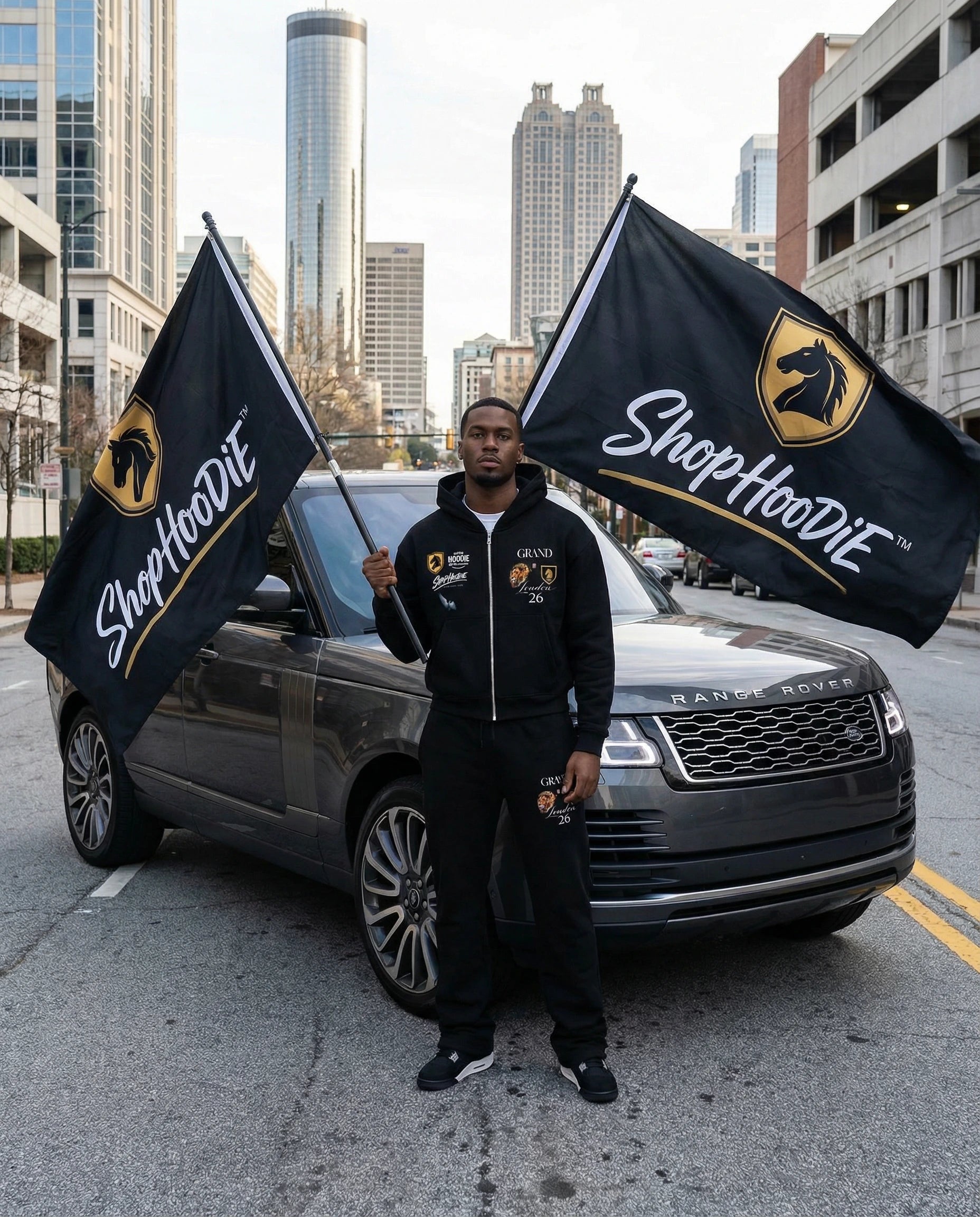 Person holding ShopHoodie™ flags in front of a Range Rover with cityscape background