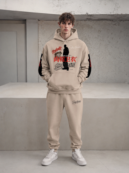 Person wearing a beige hoodie and pants with graphic designs in an indoor setting