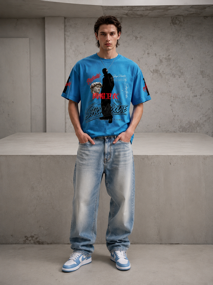 Person wearing a blue graphic t-shirt and light blue jeans standing in a minimalistic room.