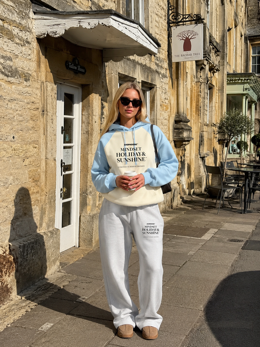 Person wearing a light blue hoodie and white pants with text, standing on a street.