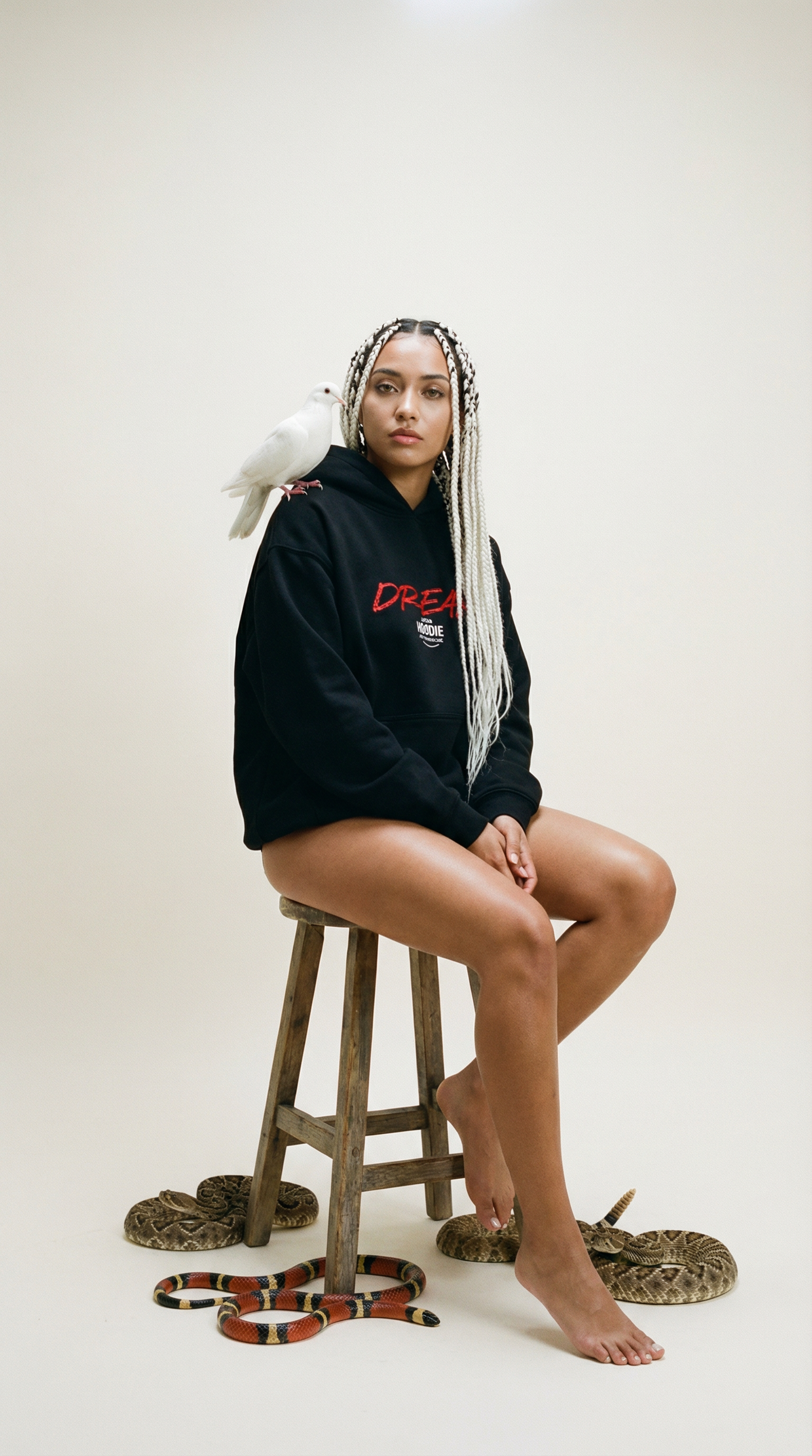 Person wearing a black hoodie with red text, sitting on a stool with snakes around, on a white background CFTDirect.com dream hoodie shophoodie.co.uk