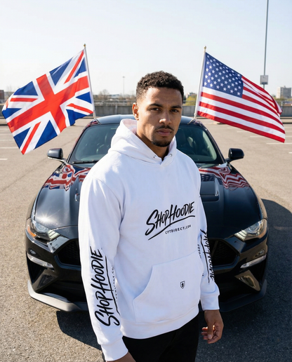 Man wearing a white hoodie with branding in front of a car with British and American flags.