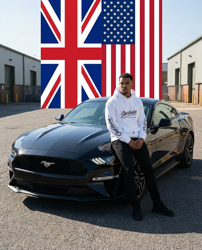 Man posing next to a black Mustang car with British and American flags in the background