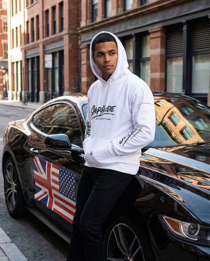 Person wearing a white hoodie with branding, standing next to a black car with British and American flags on a city street.