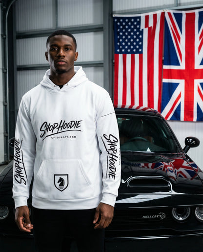 Person wearing a white hoodie with branding in front of a car and flags.