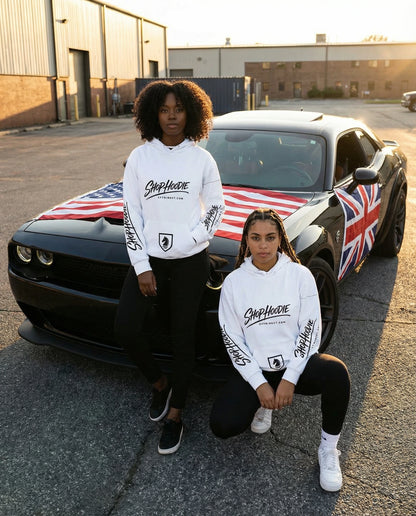 Two people wearing white hoodies with logos in front of a black car with an American and British flag design.