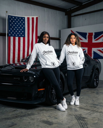 Two people wearing 'Shop Heaven' hoodies standing in front of a black car with American and British flags in the background.