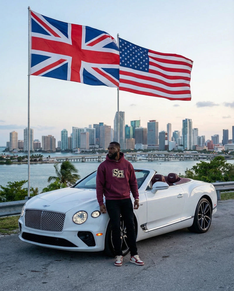 Man standing next to a white Bentley with American and British flags, city Miami skyline in the background ShopHoodie™