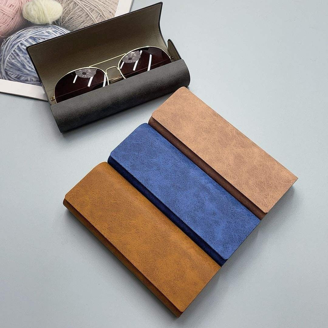 Two pairs of sunglasses in brown and blue cases on a light gray surface.