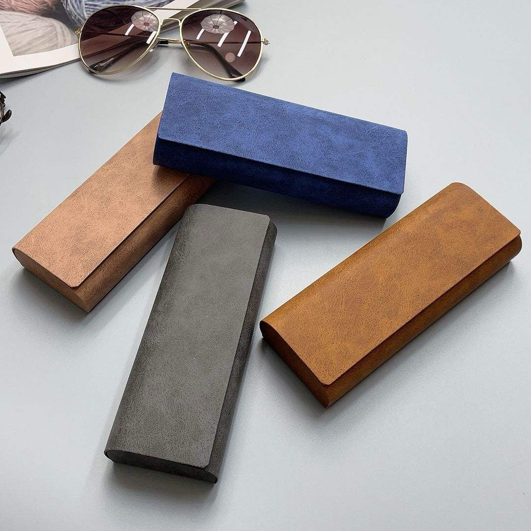 Four different colored glasses cases on a light gray surface with sunglasses in the background.
