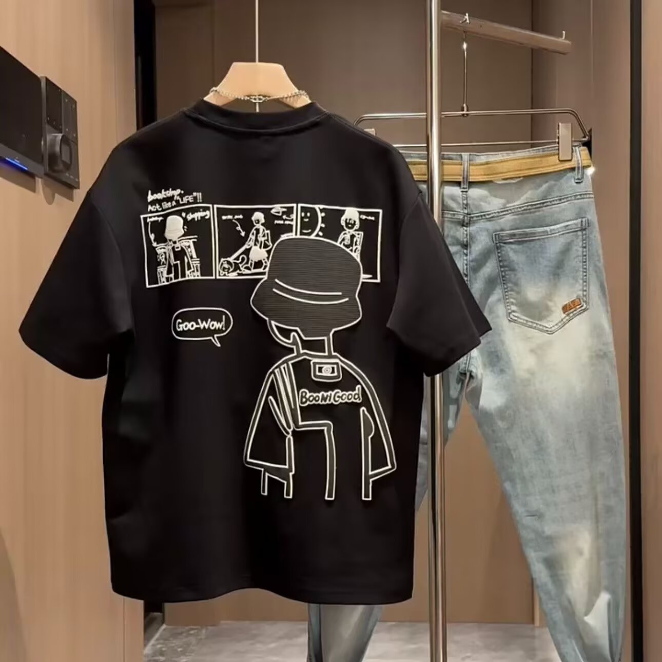 Black t-shirt with graphic design on a hanger next to light blue jeans.