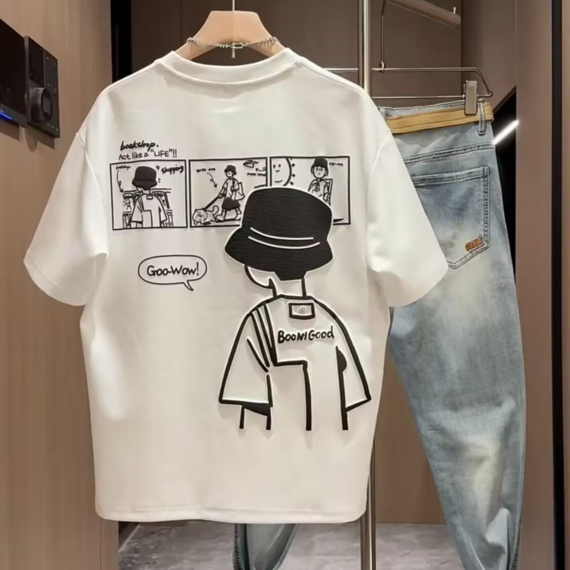 White t-shirt with black graphic design on a hanger, next to blue jeans.