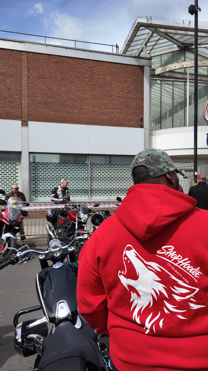 Person wearing a red shophoodie brand hoodie with a wolf design, sitting on a motorcycle in an urban setting.