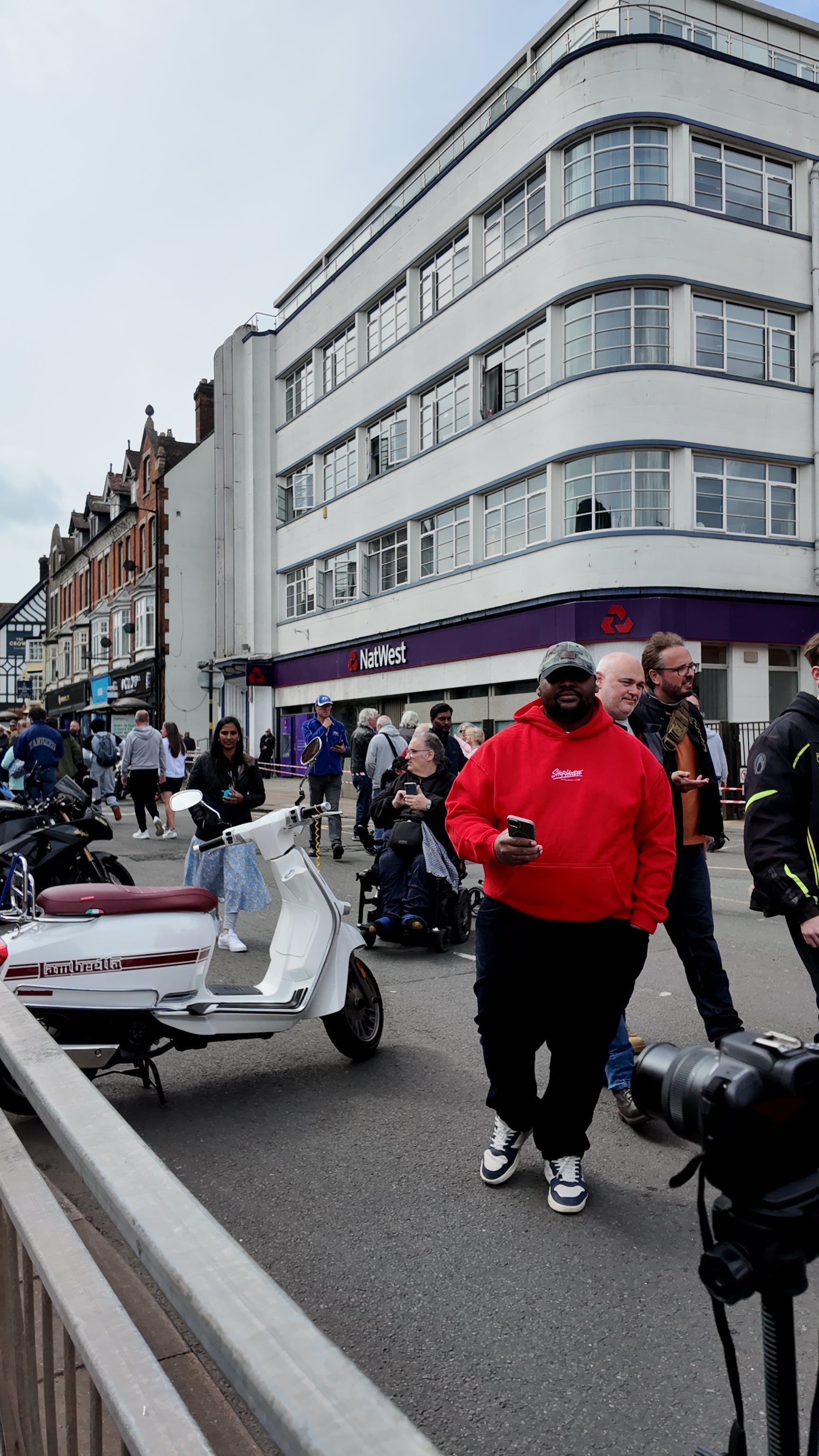 Person in a red shophoodie brand hoodie jacket walking on a street with a building and people in the background