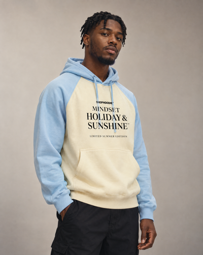 Male model wearing the SHOPHOODIE® Mindset Holiday & Sunshine Raglan Hoodie in Mild Apricot with Sky Blue – studio portrait