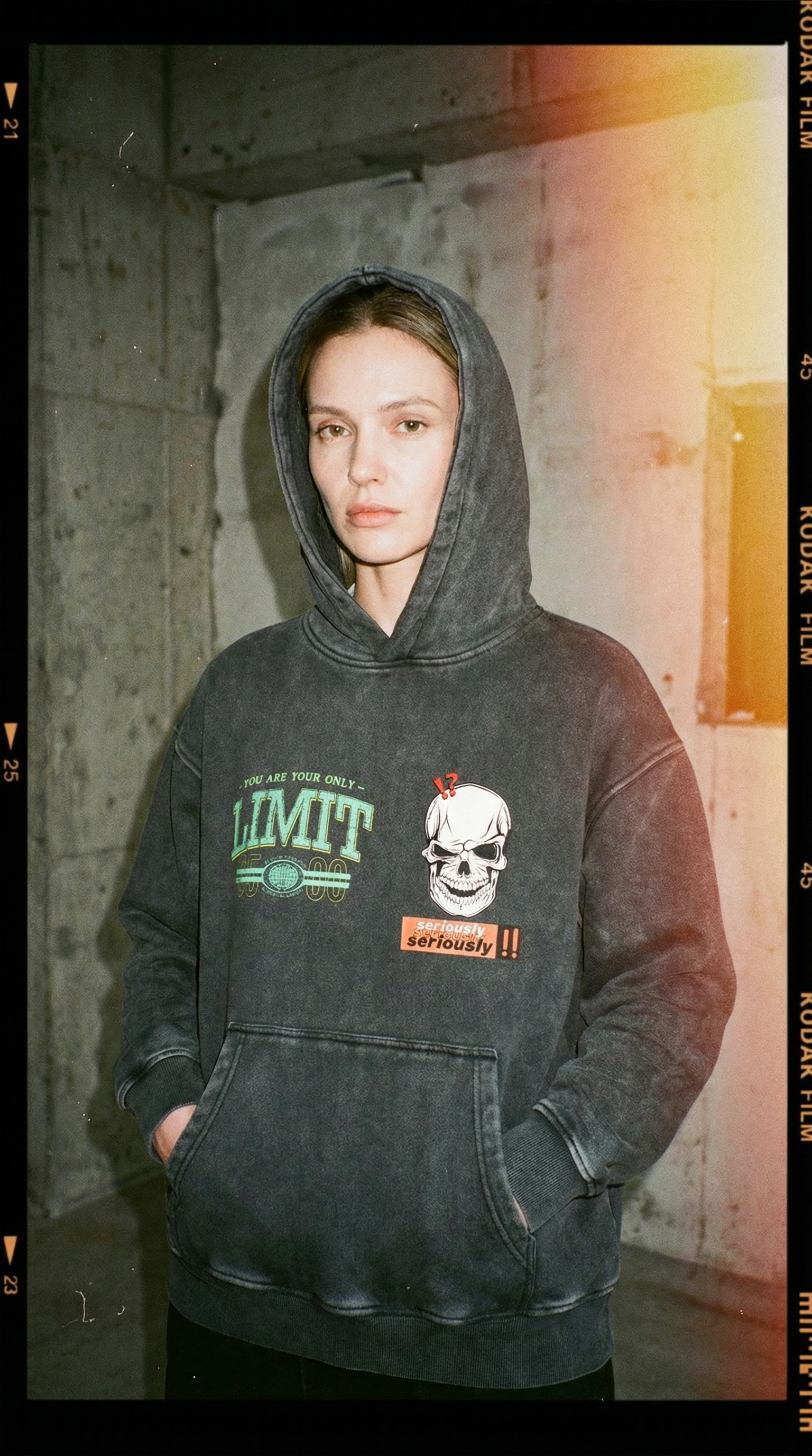 Person wearing a dark hoodie with graphic designs in an urban setting