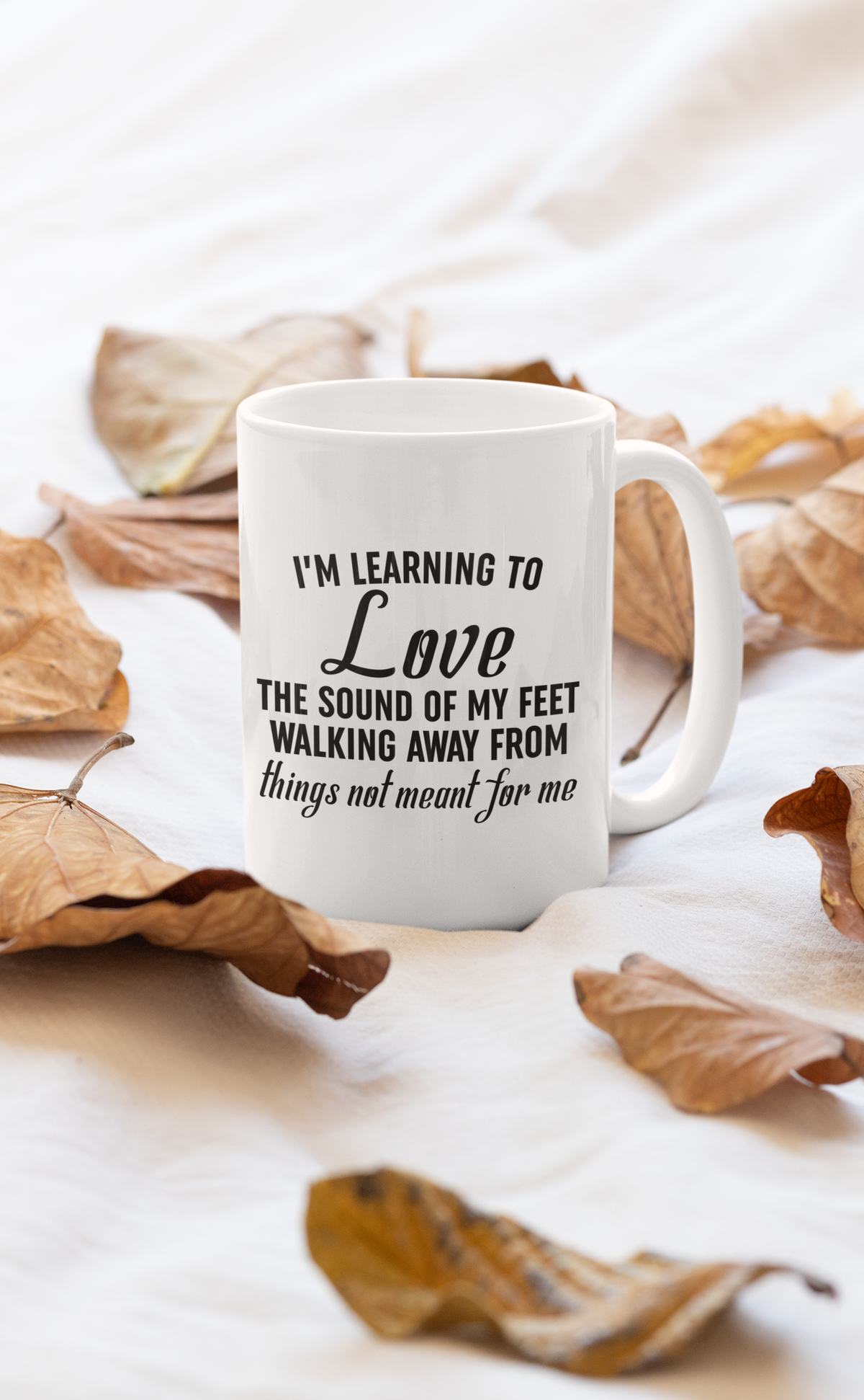 White mug with a motivational quote on a light background with dried leaves